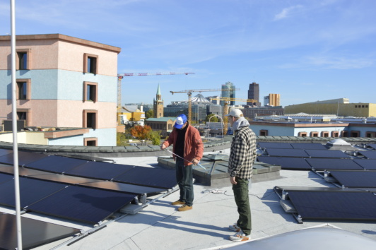 Zwei Personen prüfen auf einem Flachdach die Installation von Photovoltaikmodulen
